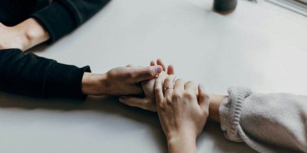 Two people holding hands on a white table, one wearing a thin ring